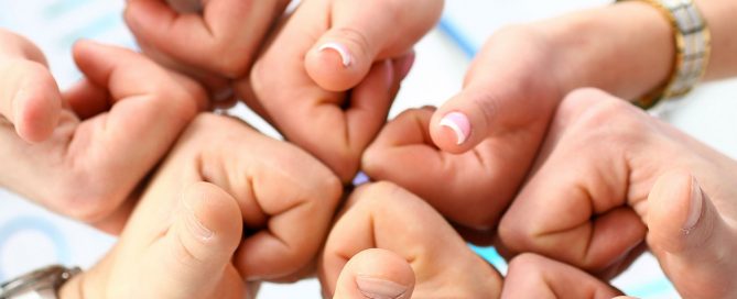 Group of people joining hands with thumbs up