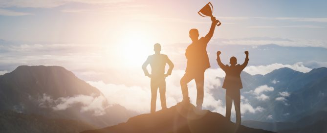 Victory Concept, Group of businesspeople on top of a mountain raising hands with a trophy